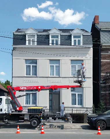 Un peintre sur une nacelle peint une façade de maison